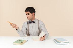 Estudante adulto sentado à mesa e apontando para o lado com uma caneta