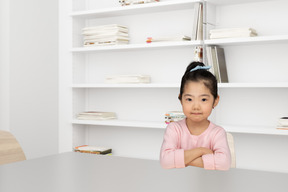A little girl sitting at a table in front of a book shelf