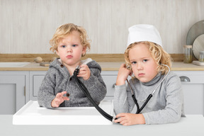 Two children sitting at a table with a stethoscope