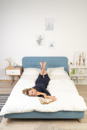 Vista frontal de uma jovem lendo livro feminino na cama