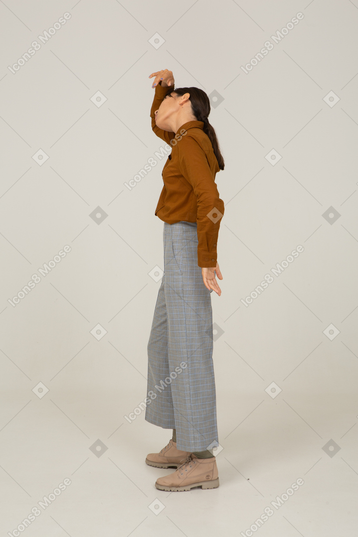 Vista lateral de uma jovem mulher asiática de calça e blusa, levantando a mão e inclinando a cabeça