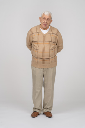Vista frontal de um velho em roupas casuais em pé com as mãos atrás das costas e olhando para a câmera