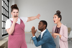 Begging man and surprised woman standing in front of woman eating donut