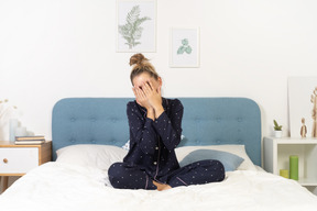 Front view of a young woman in pajamas staying in bed and hiding face