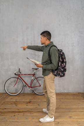 Side view of a man with a backpack looking at a map and pointing aside