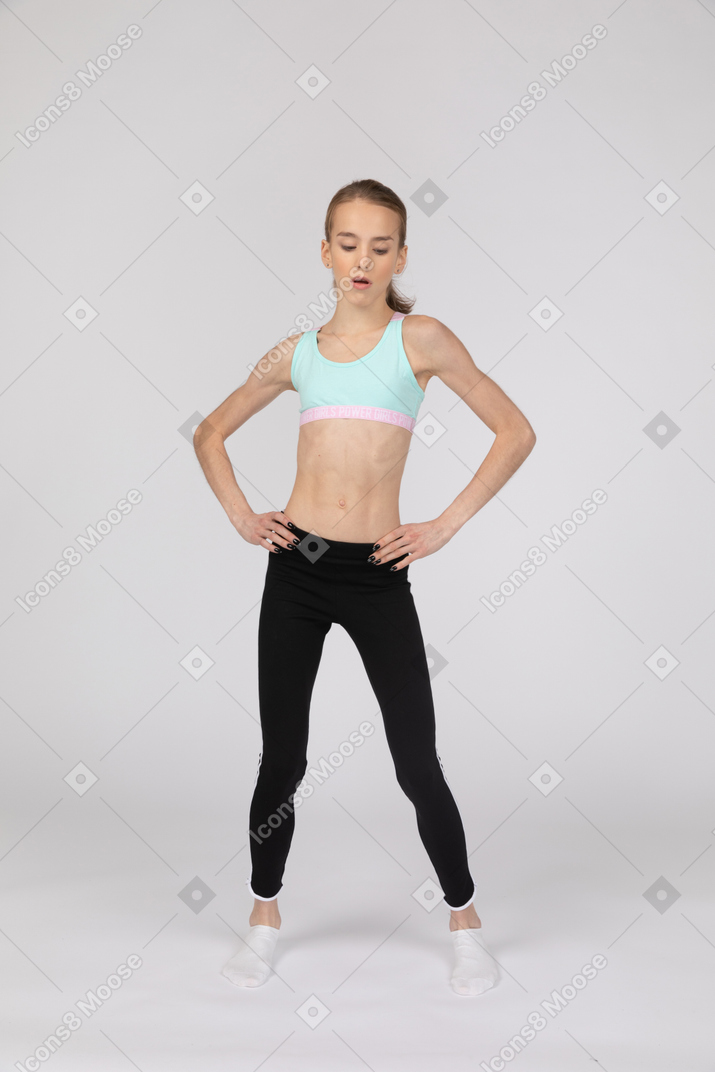 Front view of a teen girl in sportswear putting hands on hips and looking down