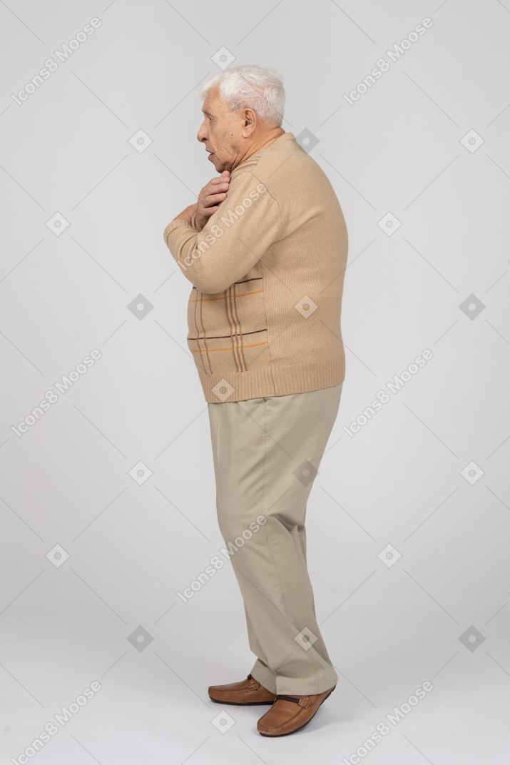 Side view of a scared old man in casual clothes standing with hands on shoulders