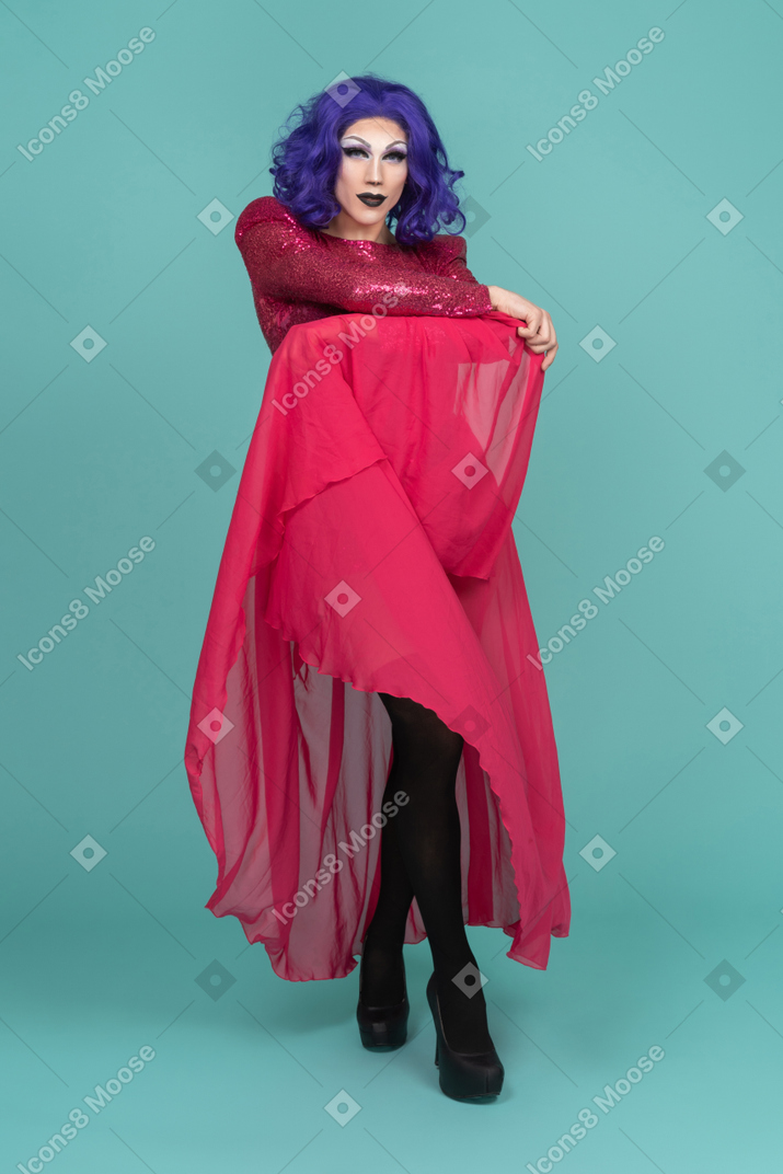 Drag queen in rosa kleid hält langen rock hoch, während sie posiert
