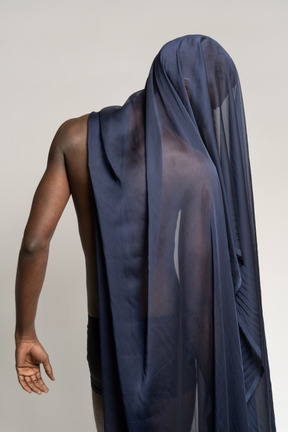 Vista posteriore di un giovane uomo afro coperto con uno scialle blu scuro guardando verso il basso