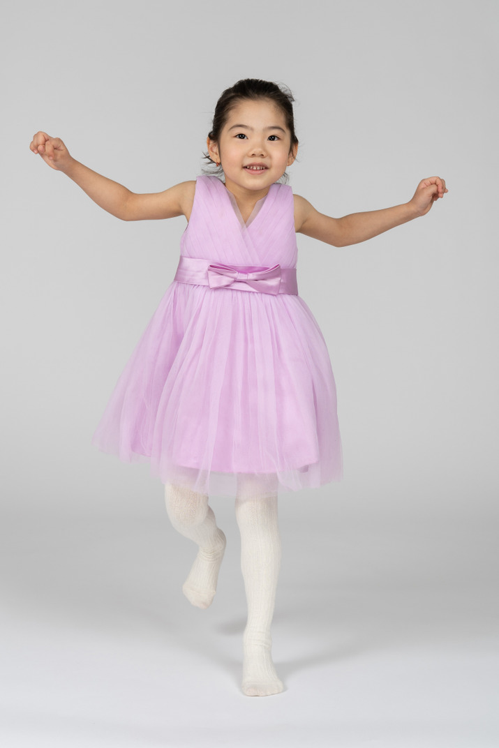 Girl in a pink dress jumping on one leg