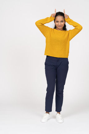 Front view of a happy girl in casual clothes making horns with fingers