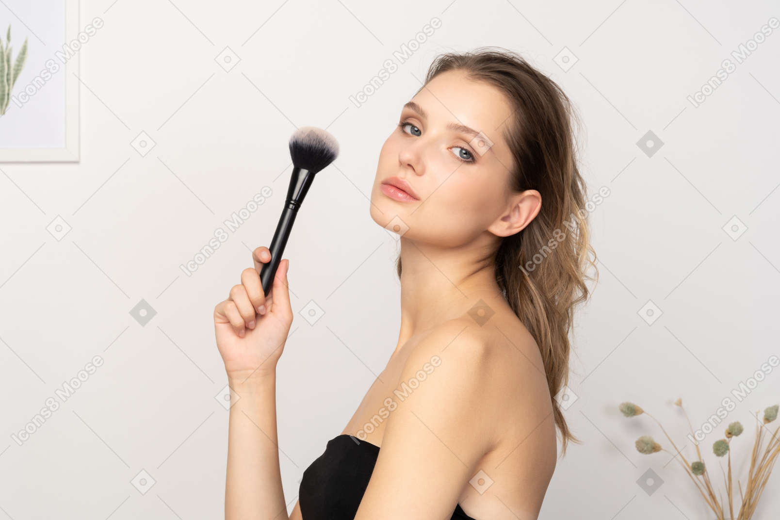 一个性感的年轻女子拿着化妆刷 & 看着相机的侧视图