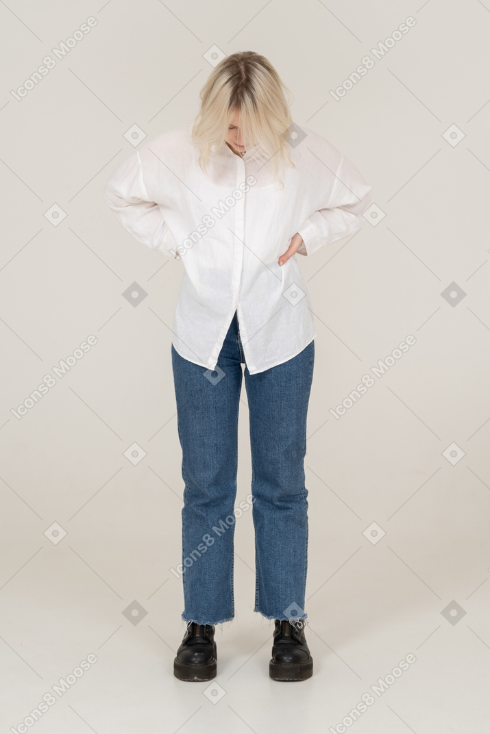 Vista frontal de una mujer rubia en ropa casual poniendo las manos en las caderas y mirando hacia abajo