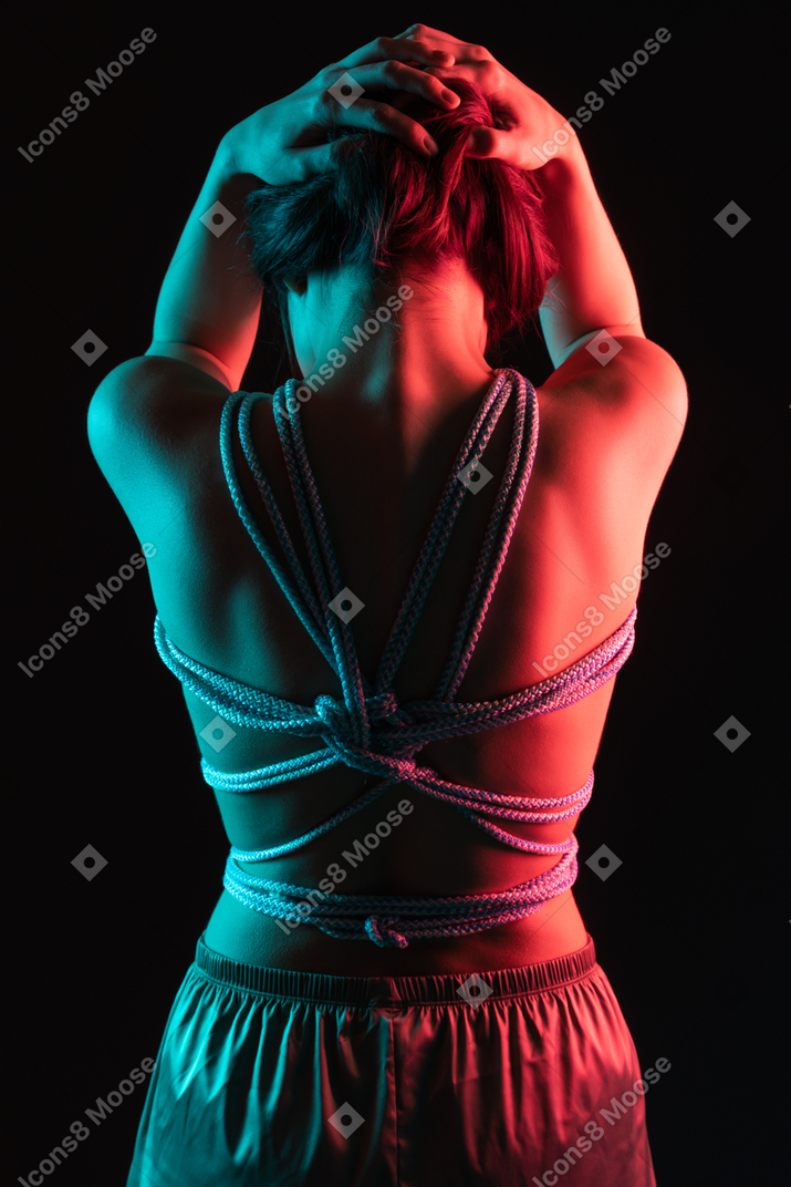 Back shot of a roped woman touching her hair in neon lights
