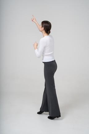 Side view of a woman in black pants and white blouse pointing up with a finger