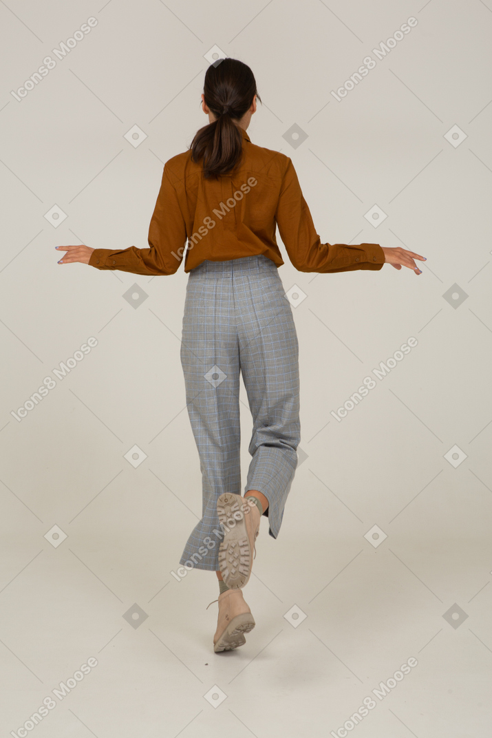 Vista posteriore di una giovane donna asiatica che salta in calzoni e camicetta che allarga le mani