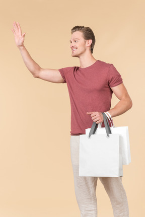 Young guy holding white shopping bags and waving