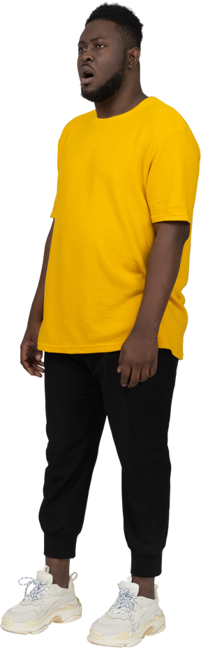 一个穿着黄色 t 恤的深肤色年轻男子惊讶地站在原地的四分之三视图