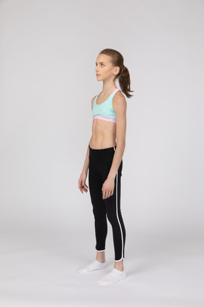 Вид в три четверти девушки-подростка в спортивной одежде, стоящей на месте и смотрящей вверх