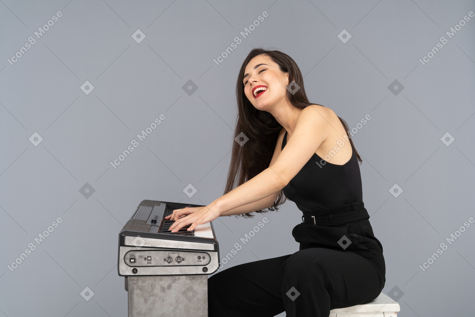 Vista laterale di una giovane donna sorridente seduta in abito nero mentre suona il pianoforte