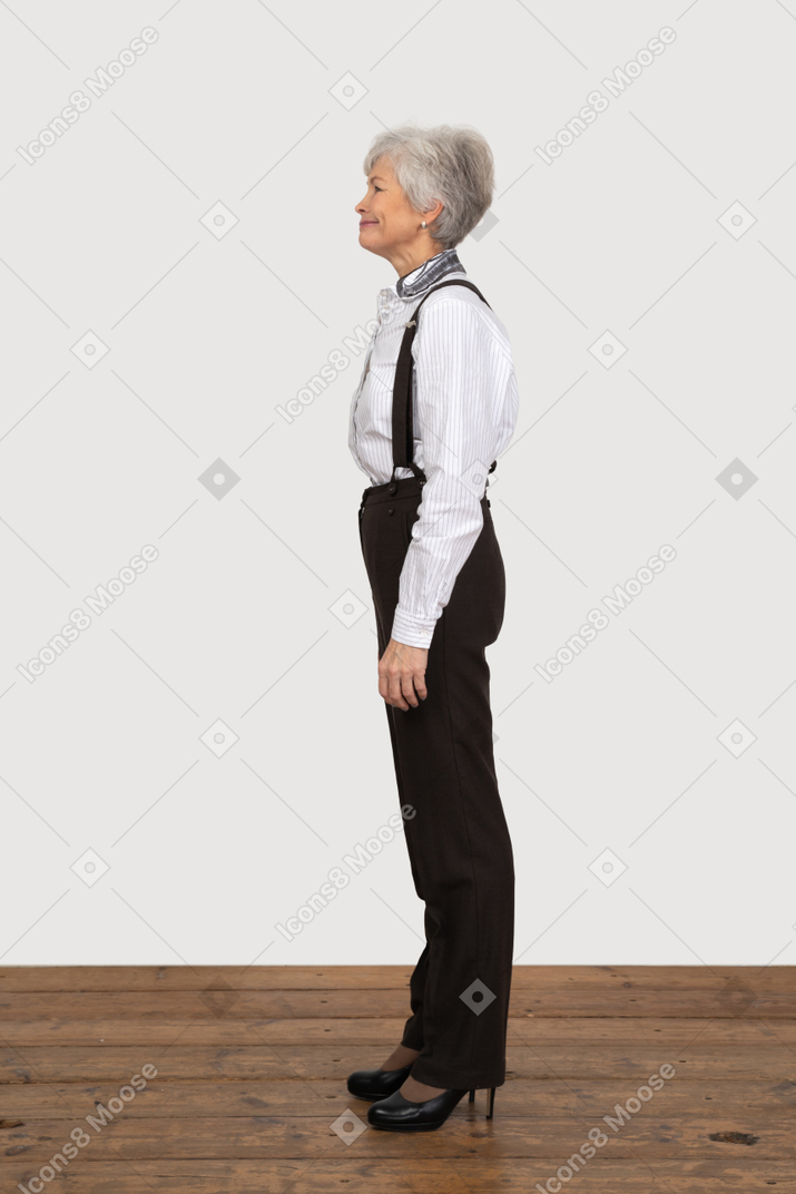 Vista lateral de uma mulher idosa com roupas de escritório, parada na sala