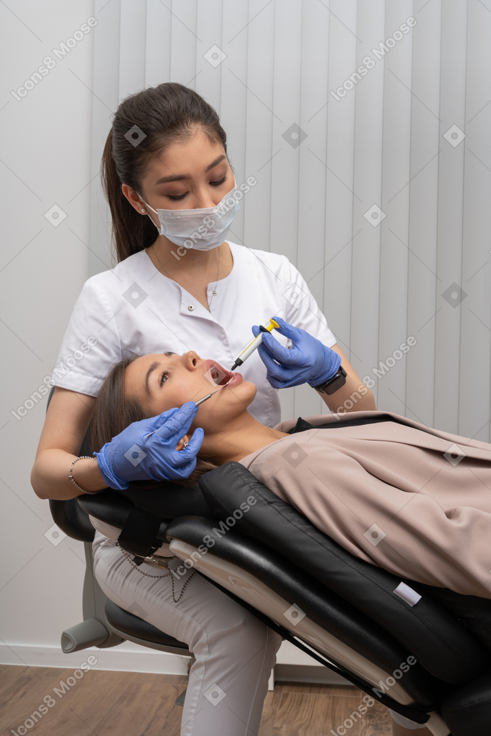 Female dentist in mask and latex gloves making injection to her patient