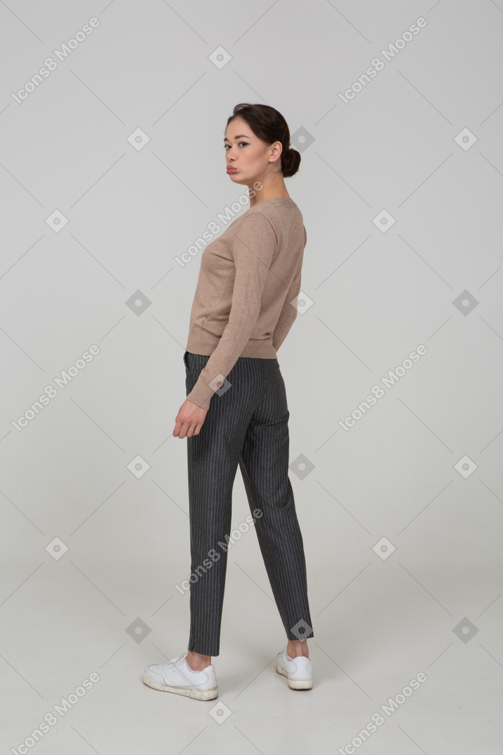 Three-quarter back view of a pouting young lady in pullover and pants turning away