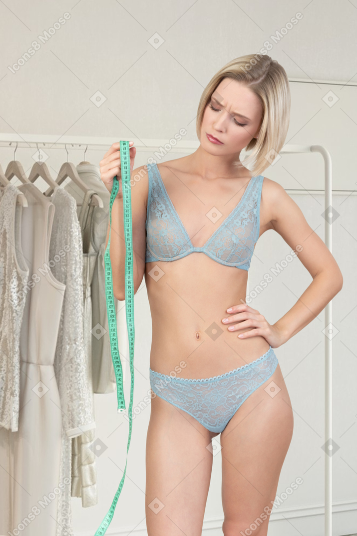 A woman in a bra and panties holding a measuring tape