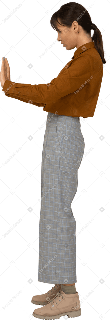 Vista laterale di una giovane donna asiatica in calzoni e camicetta che allunga il braccio