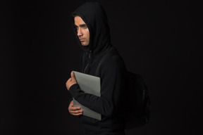 Хакер парень стоит в темноте и держит ноутбук