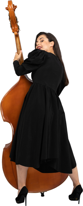 Vista de trás de uma jovem musicista satisfeita em um vestido preto segurando seu contrabaixo