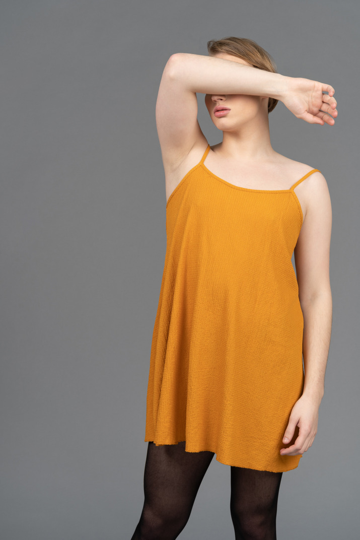 Young queer person in orange dress covering face