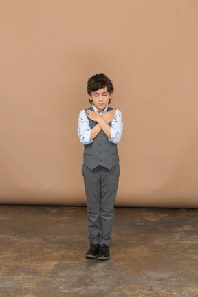 Front view of a cute boy in grey suit standing with hands on shoulders
