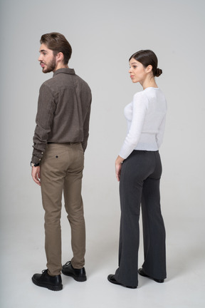 Three-quarter back view of a confused young couple in office clothing standing still