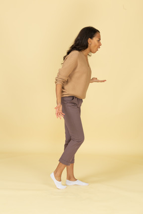 Vista lateral de una mujer joven de piel oscura cuestionando inclinándose hacia adelante