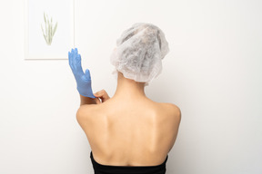 Back view of a woman putting on medical gloves