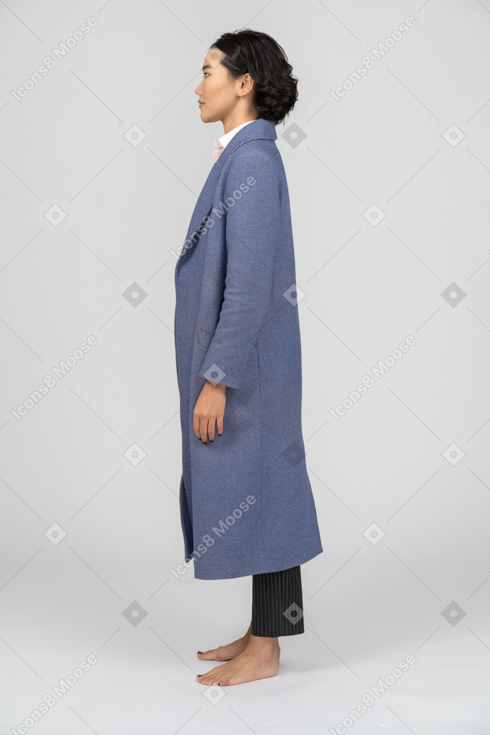 Вид сбоку на женщину в синем пальто, стоящую