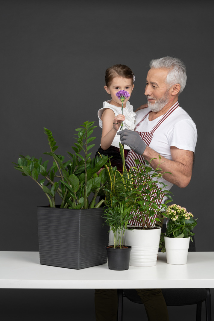 A mature man holding a little girl on his hands next to the house plants