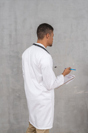 Vista traseira do médico masculino fazendo anotações
