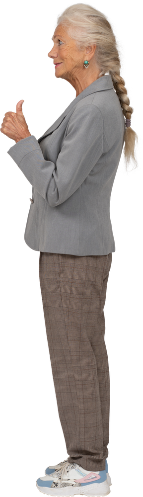 Vista lateral de una anciana feliz en traje mostrando el pulgar hacia arriba