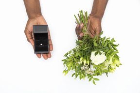 Macho preto mãos segurando buquê de flores e caixa com um anel