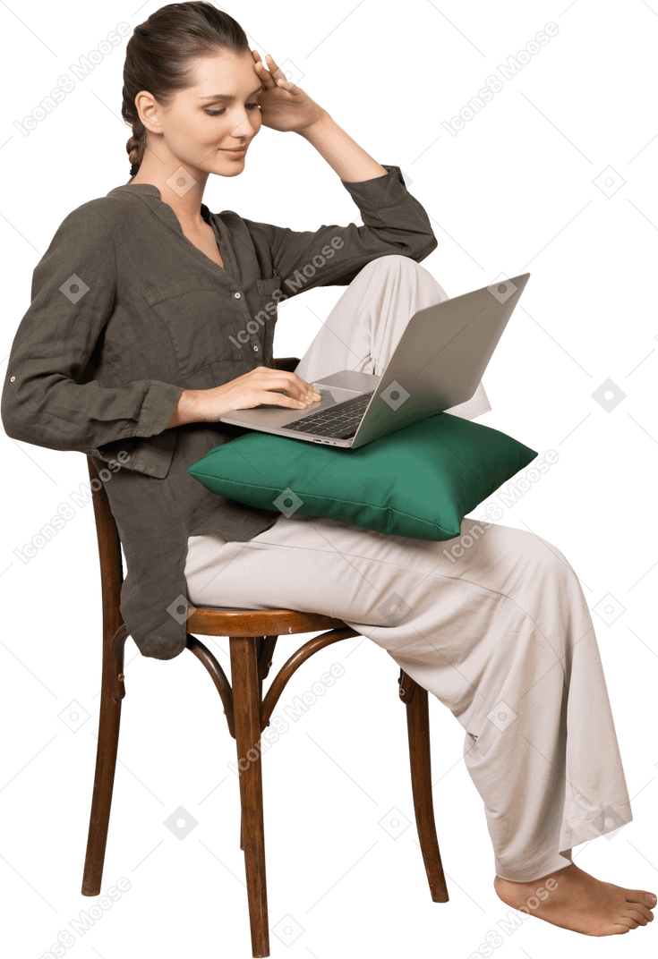 Vista de três quartos de uma jovem vestindo roupas de casa, sentada em uma cadeira com um laptop e tocando a testa