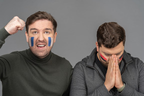 Vista frontal de dos aficionados al fútbol masculino emocional con arte facial