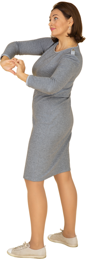 Vista laterale di una donna in abito grigio che mostra il gesto del cuore
