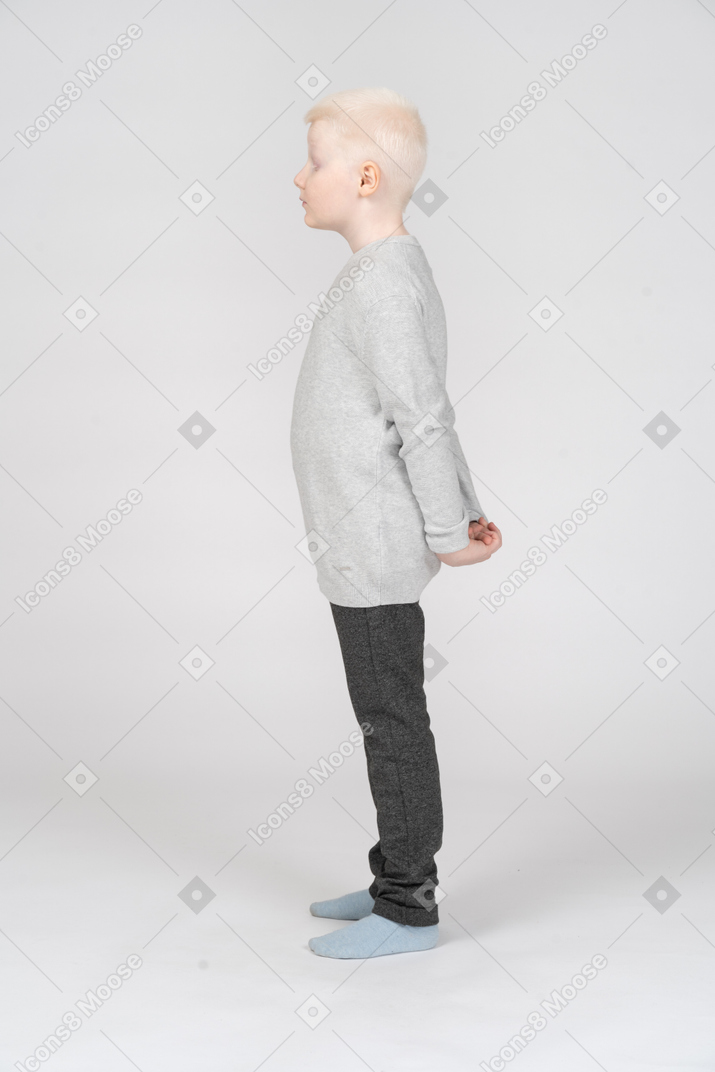 立って後ろに手を隠しているカジュアルな服を着た金髪の少年