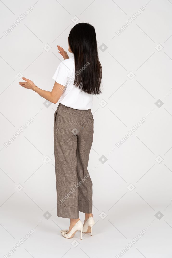 Vista traseira de três quartos de uma jovem de calça e camiseta branca mostrando o tamanho de alguma coisa