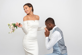 Marié embrasser la main de sa fiancée et elle tient un bouquet et souriant