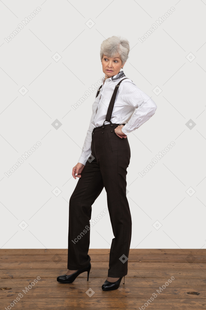 Side view of a displeased old lady in office clothing putting hand on hip