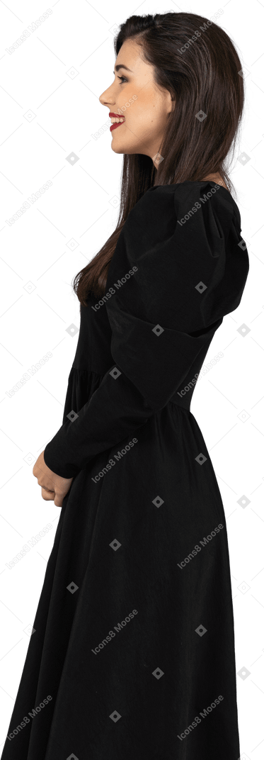 Side view of a smiling young lady in a black dress standing still