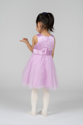 一个穿着芭蕾舞短裙的小女孩的后视图，她的拇指指向右边